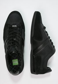 Pari musta BOSS-kesäkenkiä nauhakiinnityksellä, verkko- ja mokkanahkateksillä sekä brändätyillä sisäpohjilla valkoista taustaa vasten.