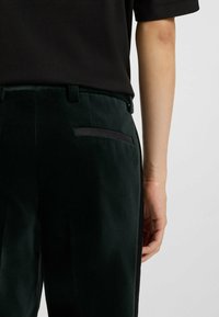 Grüne Saminhosen mit glatter Textur, ausgestattet mit einer eleganten Gesäßtasche mit schwarzem Besatz und einem taillierten Schnitt.