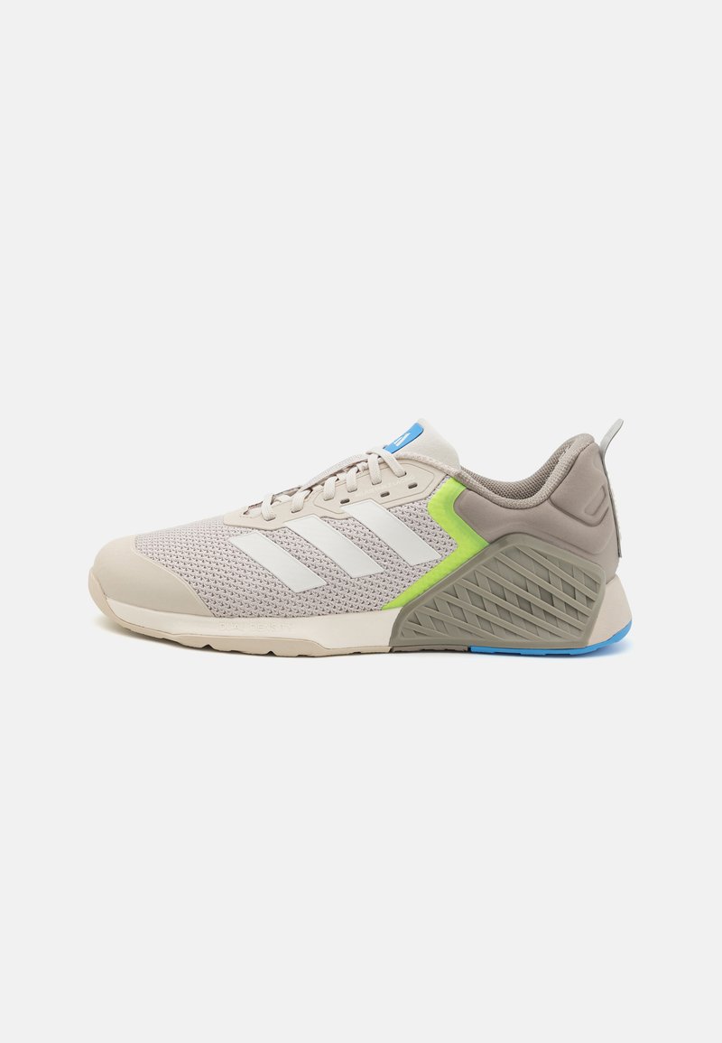 Light beige sneaker with mesh upper, white stripes, green accent on the heel, and textured grey sole. Features blue logo on the tongue.