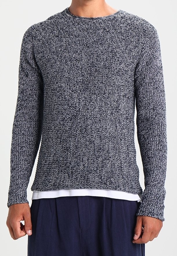 Marineblauer und grauer Strickpullover mit langen Ärmeln, rundem Halsausschnitt und strukturiertem Muster; getragen über einem weißen, mehrlagigen Hemd.