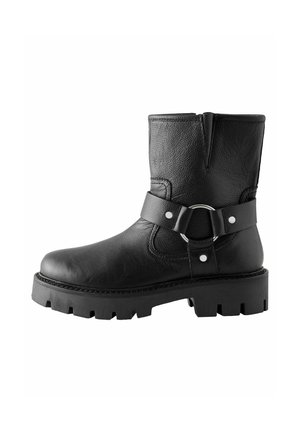 Bottine en cuir noir avec une finition texturée, dotée d'une sangle à boucle en argent ronde, d'un embout renforcé et d'une semelle épaisse noire avec des crampons.