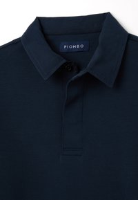 Dunkelblaues Poloshirt mit klassischem Kragen, Knopfverschluss und subtiler Textur. Markenlabel "PIOMBO" innen am Kragen.