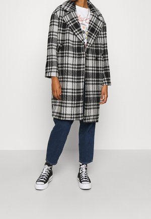 Black and white plaid coat with large lapels, mid-length sleeves, and a loose fit, paired with dark blue jeans and black sneakers.