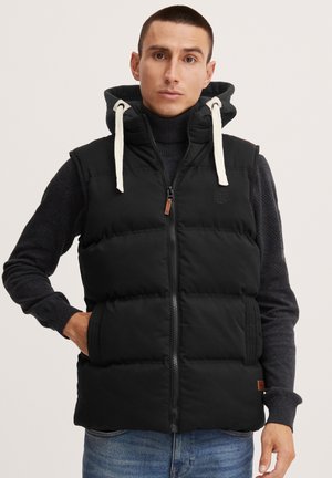 Zwarte puffer vest met capuchon, ritsluiting, crèmekleurige koordjes en zijzakken. Textuurstof met een doorgestikt ontwerp, merklogo op de borst.