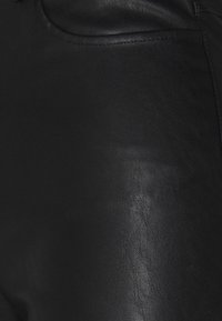 Gros plan d'un tissu en cuir noir lisse avec un détail de couture visible le long d'une couture courbe.