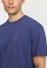 Navy blue cotton t-shirt with a round neckline and short sleeves. Features a small embroidered ketchup bottle design on the chest.