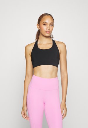 Schwarzer Sport-BH mit weitem Halsausschnitt und Racerback-Design, kombiniert mit hochgeschnittenen, figurbetonten rosa Leggings. Glatte Textur, minimale Details.