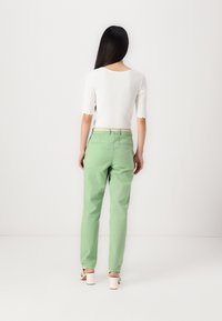 Light green cotton pants with a straight-leg design, worn with a white top featuring scalloped sleeves. Simple belt and neutral shoes.