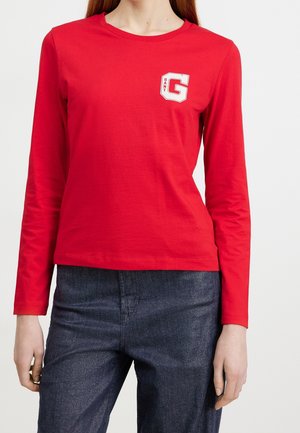 Rød langærmet T-shirt lavet af bomuld med rund hals og et hvidt G-logo på venstre bryst. Kombineret med mørkeblå teksturerede bukser.