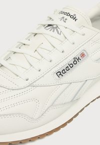 Baskets en cuir blanches Reebok avec lacets blancs, logo de la marque sur le côté et la languette, et semelle couleur gomme.