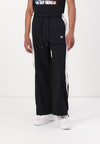Svarta vida träningsbyxor med vita sidopaneler, dragsko i midjan och Nike-logga på nedre benet. Gjorda av lätt material.