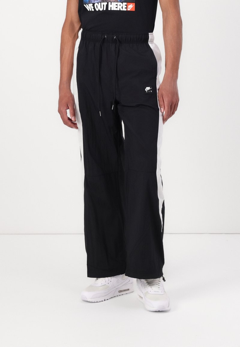 Svarta vida träningsbyxor med vita sidopaneler, dragsko i midjan och Nike-logga på nedre benet. Gjorda av lätt material.