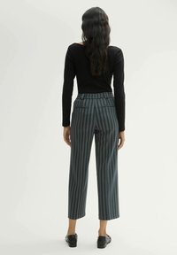 Wijduitlopende broek met een blauw-wit verticale streep patroon. Heeft een hoge taille en twee achterzakken. Gecombineerd met een zwart shirt.