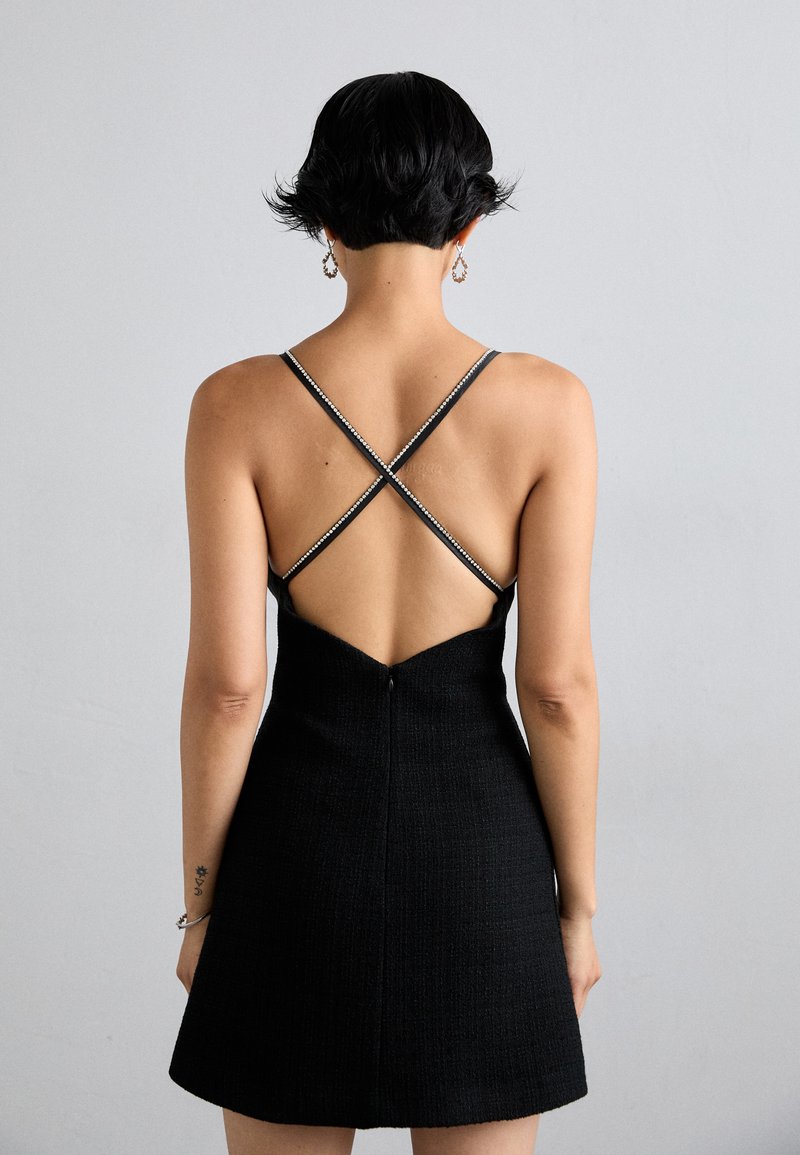 Schwarzes A-Linien-Kleid mit strukturierter Oberfläche, gekreuzten Trägern im Rücken und einem tiefen V-Ausschnitt hinten, der mit einem verdeckten Reißverschluss versehen ist.