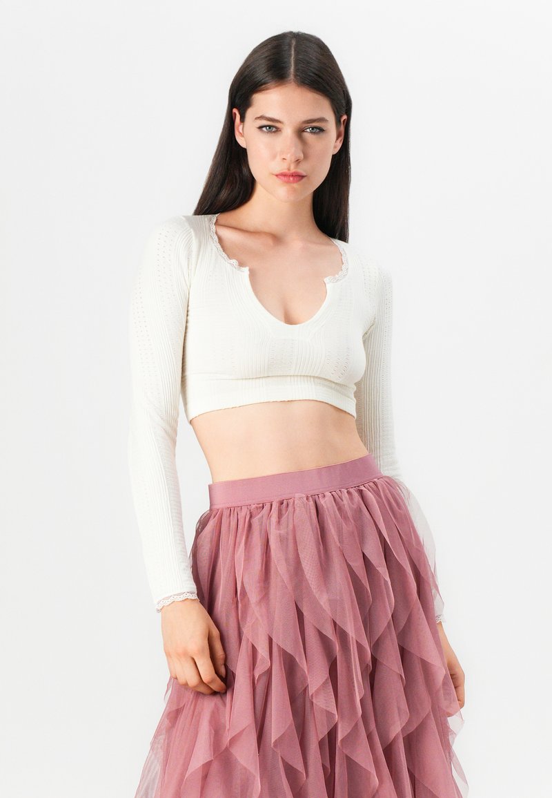 Weißes geripptes Crop-Top mit Spitze am Halsausschnitt und langen Ärmeln, kombiniert mit einem geschichteten pinken Tüllrock mit einem breiten Taillenbund.