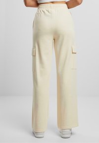 Sweatpants širokih nogavica boje kreme, izrađeni od mekog materijala, s dva bočna džepa za teret i elastičnom pojasom.