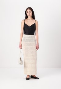 Un haut en satin noir à fines bretelles associé à une longue jupe en tricot texturé crème, accentuée par des rayures horizontales, et des chaussures plates noires.