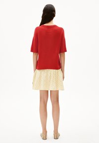 Rode ribbed top met korte mouwen, gecombineerd met een gele rok met een licht stippenpatroon. Eenvoudig ontwerp, relaxte pasvorm en textuurstof.