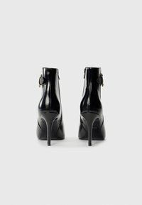 Sorte lakk lær ankelstøvler med spiss tå, høye stiletto-heler og glidelåslukking på siden. Detaljer i gullton.