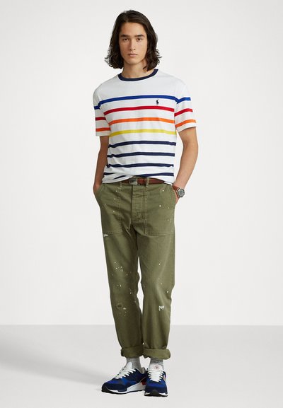 Striped white T-shirt with red, orange, yellow, and navy bands, olive green cargo pants with distressed details, and navy sneakers.