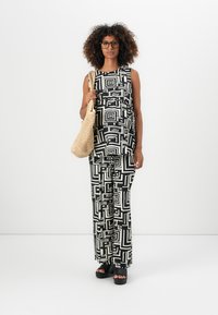 Svart og hvitt mønstrete jumpsuit med geometriske design, vide bukser og ermeløs topp. Kombinert med en vevd veske og platåsandaler.