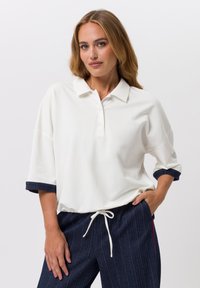 Polo blanc à manches courtes avec patte de boutonnage et poignets à rayures en denim, associé à un pantalon rayé bleu marine avec taille à cordon.