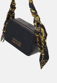 Borsa rettangolare nera di Versace Jeans Couture con zip dorata e logo, dotata di due manici in tessuto nero e dorato a motivo, annodati.