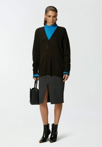 Crna kardigan jakna s gumbima, plavi rolak, siva olovka suknja s prednjim prorezom, crne čizme do gležnja s metalnim akcentima i crna torba.