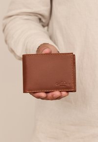 Brązowy skórzany portfel o gładkiej teksturze, w układzie bi-fold, z widocznym przeszyciem i wytłoczonym logo na powierzchni. Kompaktowy rozmiar do trzymania w ręce.