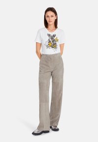 Weißes T-Shirt mit einem Koala-Graphic, graue hochgeschnittene Wildlederhose und metallische Plateauschuhe. Einfaches Design, weicher Stoff.