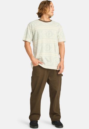 Light-colored patterned short-sleeve shirt with a round neck, paired with brown loose-fitting pants and black sneakers.