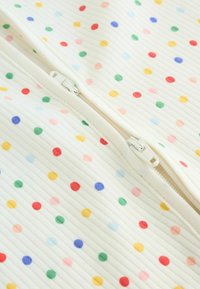 Gros plan sur un tissu blanc côtelé à pois multicolores avec une fermeture éclair blanche partiellement fermée.