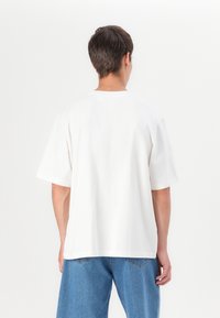 White cotton t-shirt with a relaxed fit, crew neckline, and short sleeves, displayed from the back against a plain background.