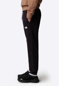 Zwarte sweatpants met een trekkoord in de taille en zijzakken, met een wit "The North Face" logo op de dij, gecombineerd met zwarte sportschoenen.