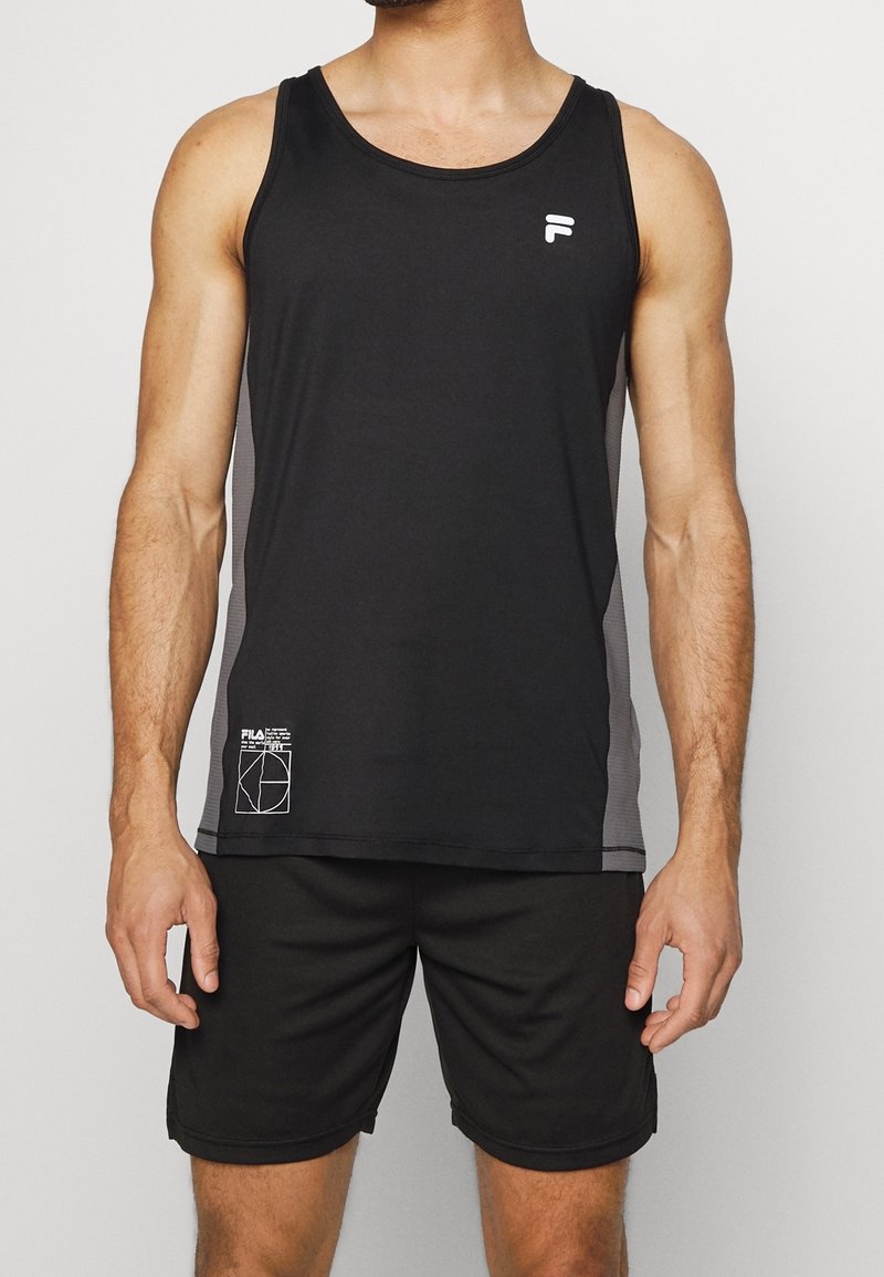 Homme portant un débardeur de sport noir sans manches et un short noir assorti, debout devant un fond uni.