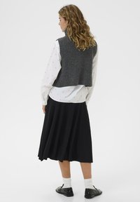 Sivi pleteni prsluk preko bijele bluze s točkicama, u kombinaciji s lepršavom crnom suknjom i crnim cipelama, prikazuje opušten i slojevit izgled.