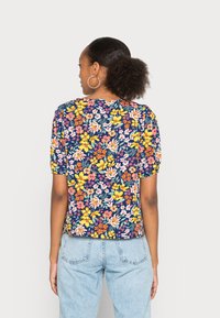 Top curto de mangas curtas com fundo azul marinho, apresentando flores amarelas, rosas e brancas. Tecido suave, corte descontraído, design cropped.