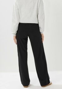 Pantalones anchos negros de tela suave, con una cintura alta y aberturas en los lados del dobladillo. La modelo lleva un sudadera corta de color gris claro.