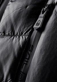 Black pufferjakke-sektion med et elegant design, tekstureret stof med et diskret gittermønster og kontrasterende lynlåsdetalje på siden.