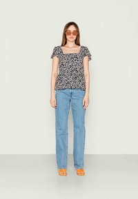 Top preto com estampa floral, com mangas curtas e pregueadas, combinado com jeans de perna reta azul claro e sandálias laranjas de bico quadrado.