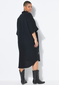 Zwarte oversized jurk met een kraag, korte mouwen en geborduurde details aan de zijkant; gecombineerd met zwarte cowboylaarzen.