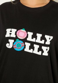 Mustat t-paidat, joissa on rohkeaa valkoista tekstiä "HOLLY JOLLY" ja värikkäitä joulupallon grafiikoita vaaleanpunaisena, sinisenä ja vihreänä. Pehmeä rakenne.