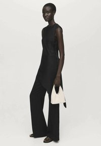 Top negro sin mangas combinado con pantalones de pierna ancha, con una silueta limpia; sosteniendo un pequeño bolso blanco con un diseño curvado.