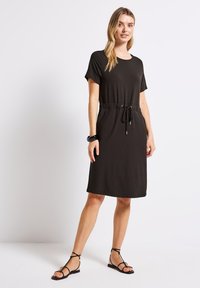 Musta polvipituinen mekko pehmeästä kankaasta, jossa on lyhyet hihat, kuminauha kireällä vyötäröllä ja rento istuvuus.