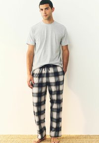 Grå kortärmad t-shirt i kombination med rutiga pyjamasbyxor i marinblått, vitt och grått, med elastisk midja och snöre.