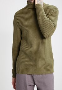 Maglione a dolcevita a coste verde oliva con design aderente e finitura texturizzata, caratterizzato da un colletto aderente e maniche lunghe.