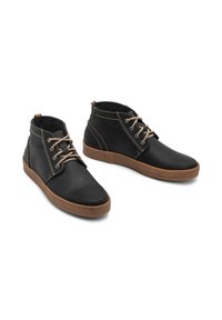 Zwarte leren enkelboots met beige veters, rubberen zool, contrasterende stiksels en een gekleurde accent bij de hak.