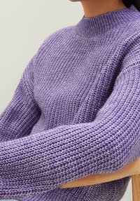 Pull-over en maille de couleur violet clair, avec un col montant, un tissage texturé et une coupe décontractée. Les poignets sont légèrement surdimensionnés avec une finition côtelée.