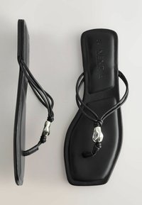 Sandales plates noires avec un bout carré, des fines double sangles et un détail de perle argentée sur chaque sangle.