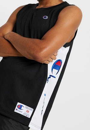 Person trägt ein schwarzes ärmelloses Champion-Sporttrikot mit weißen Seitenpaneelen und blau-rotem Logo, die Arme vor der Brust verschränkt.